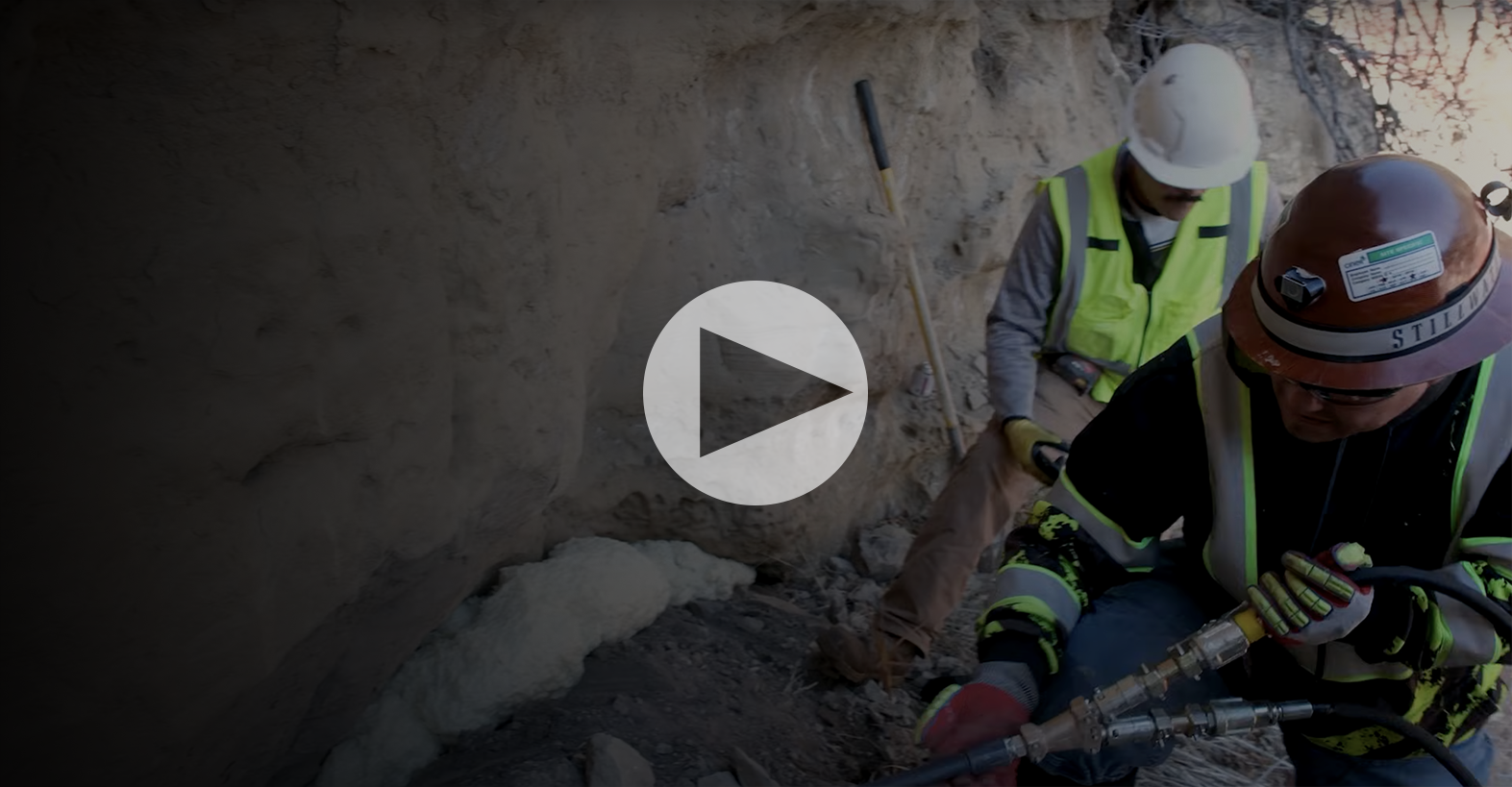 Thumbnail for a video showing two construction workers, one injecting foam into a wall and another kneeling nearby.
