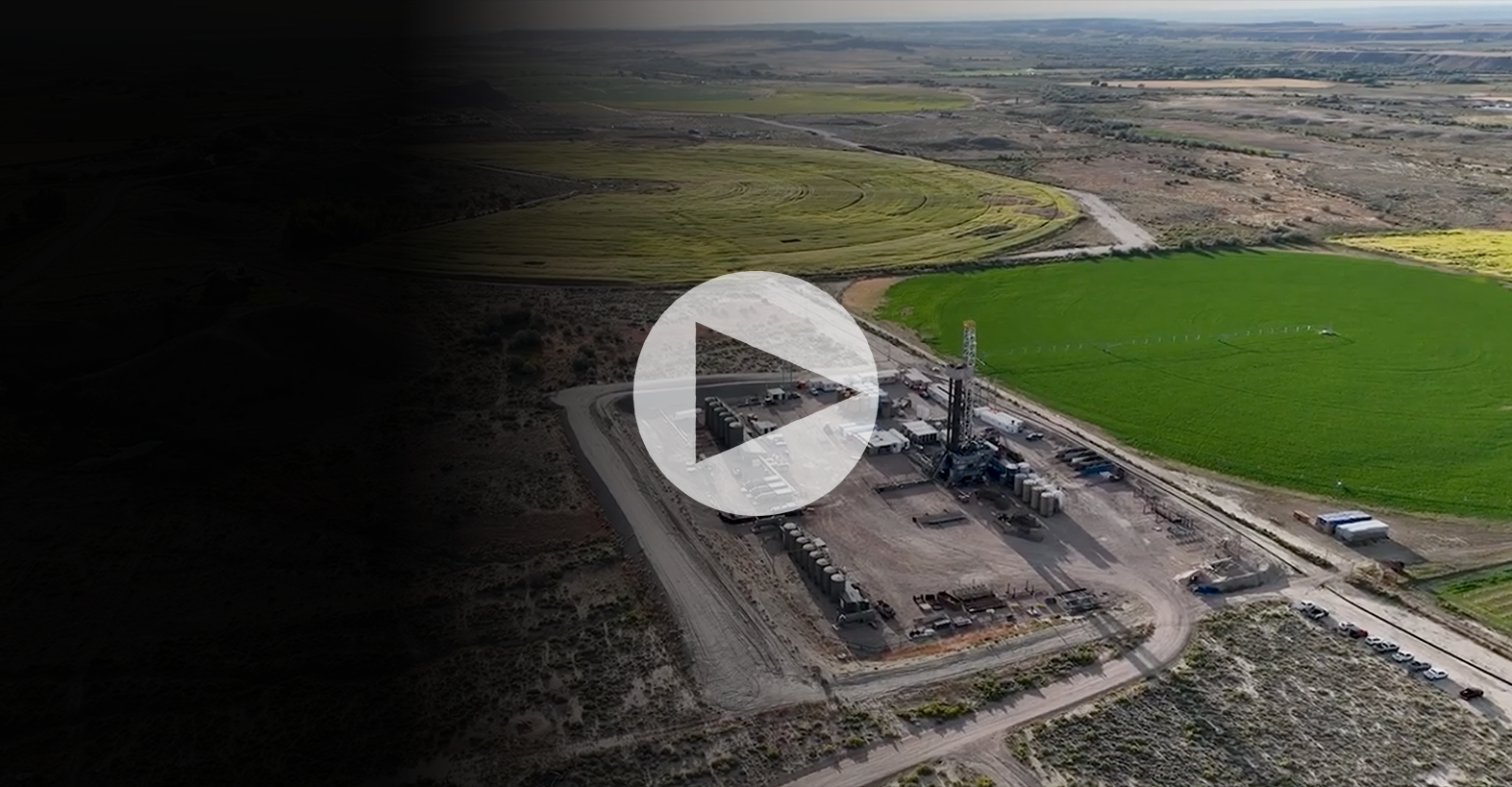 Aerial view of an industrial facility next to circular green farmland with a video play icon.